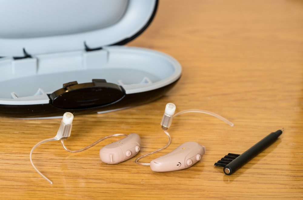 A new pair of hearing aids from Oliveira Audiology & Hearing Center with a cleaning brush lying next to them