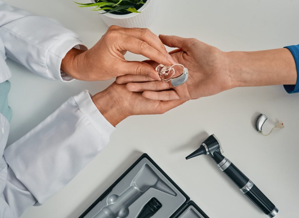 Audiologist puts modern BTE hearing aid in patient hand for treatment deafness at hearing clinic.